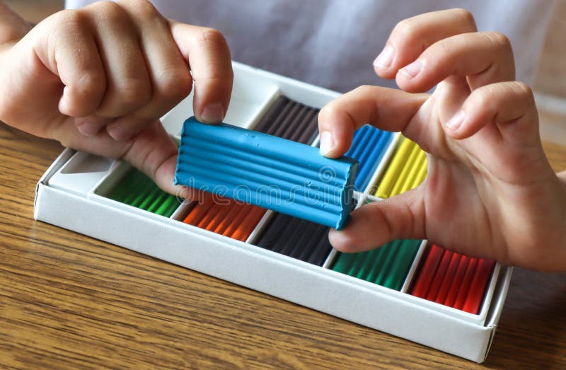 Blue plasticine in the hands of a child on the background of a box with plasticine, close-up. Blue plasticine in the hands of a child on the background of a box stock photos