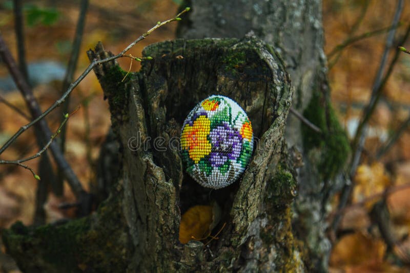 Braided egg with beads with a pattern of purple flowers. On a stump in the park. Needlework, blank.  royalty free stock photos