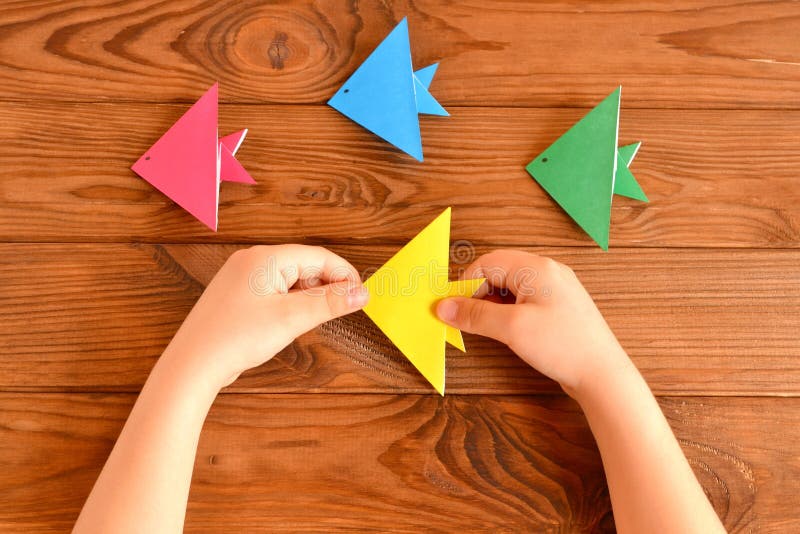 Child holds a origami fish in his hands. Set of colorful origami fish on a wooden table stock photos