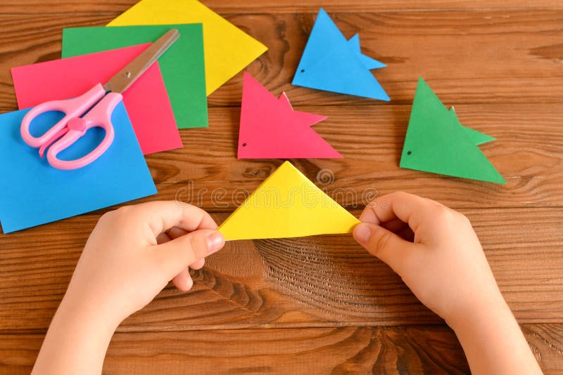 Child holds paper sheet in his hands and making origami fish royalty free stock photo