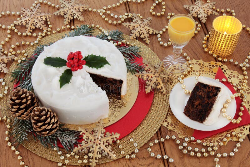 Christmas Cake and Egg Nog. Christmas cake and slice, with egg nog, holly berries, candles, gold bauble snowflake decorations with bead strands over oak table royalty free stock photo