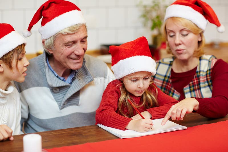Christmas drawing. Cute little girls drawing something with red pencil on page of notepad with her grandparents and brother near by stock photos