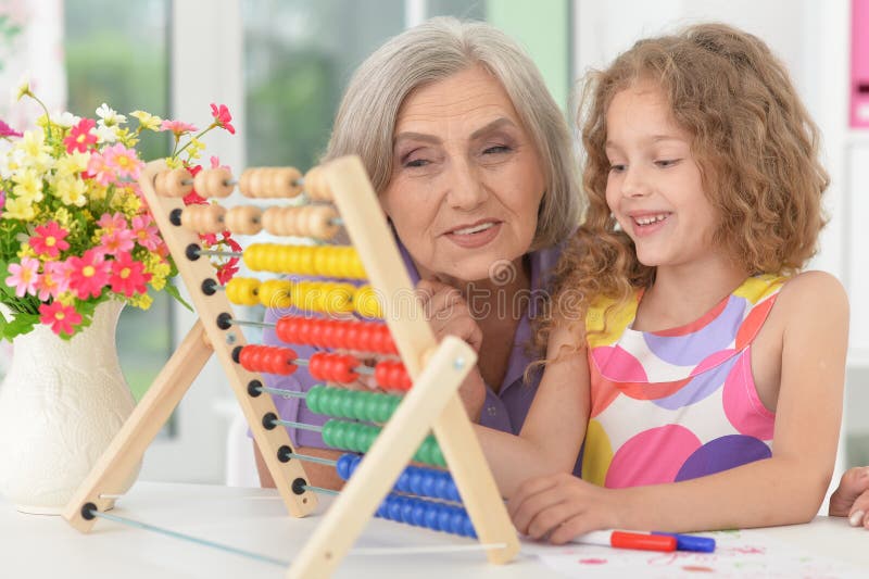 Portrait of cute schoolgirl studying with grandmother. Cute curly schoolgirl studying with grandmother in her room royalty free stock image