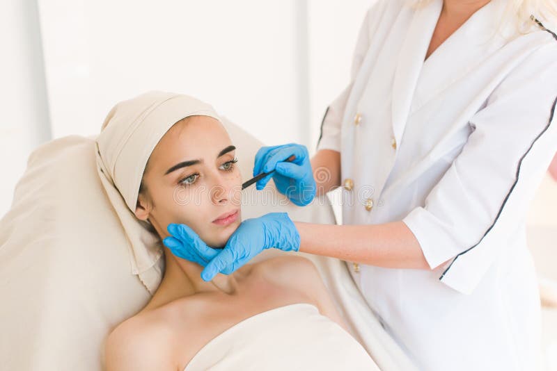 Doctor drawing marks on female face. Plastic surgery concept. Doctor drawing marks on female face against white background stock photo