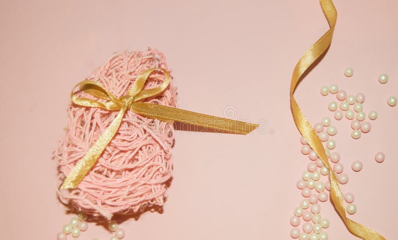 Easter egg is made of jute fiber and tied with a gold ribbon, beads on a pink background, flatlay, Easter background. Top view stock photo