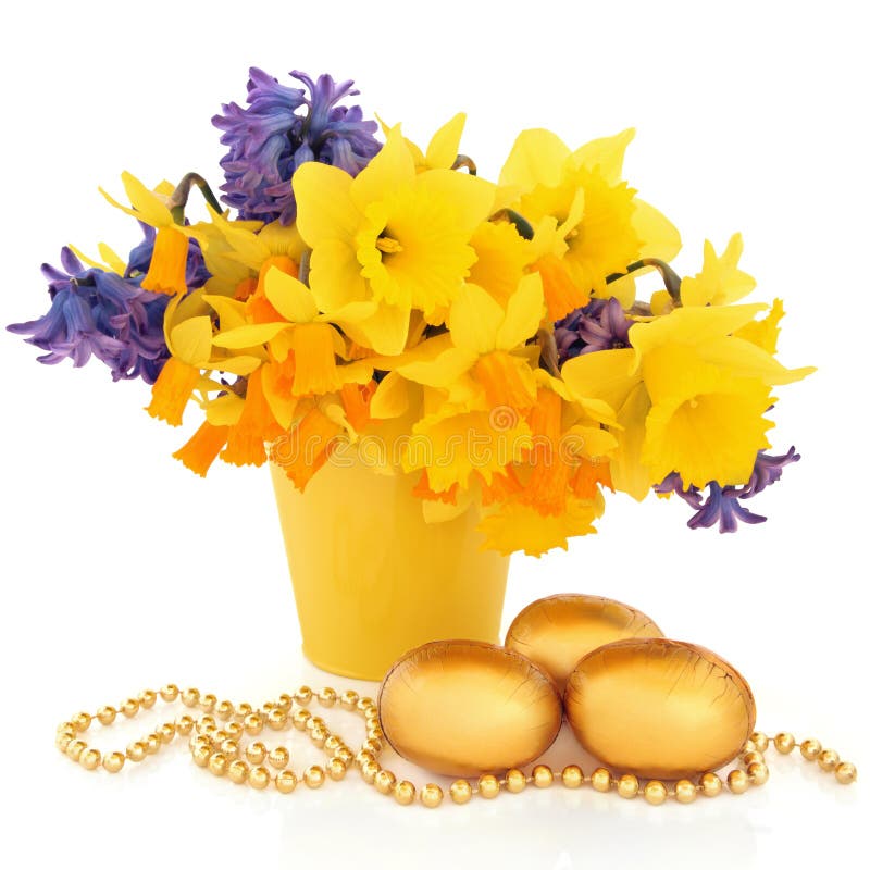 Easter Floral Display. Narcissus, daffodil and hyacinth flower arrangement in a yellow vase with a gold chocolate easter egg group and bead chain over white stock photo