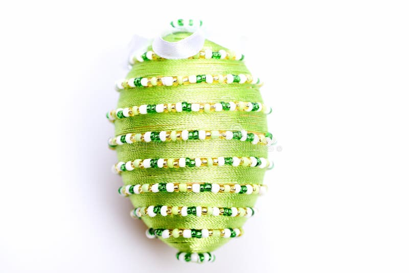 Egg decorated with thread and white beads in lines. Isolated on white background. Easter symbol and decor. Easter egg in light green color, close up. Easter day royalty free stock photo