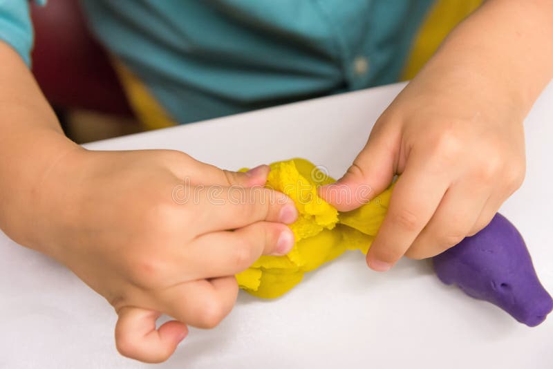 Four year old caucasian boy makes with hands animal figures from modeling yellow clay on white tabletop. Kids creativity preschool stock photos