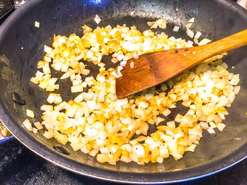 Frying Diced Onions. In skillet using a wooden spoon to stir them royalty free stock photography