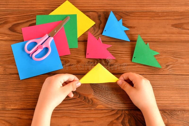 Origami colorful fish, paper sheets, scissors. Child holds paper sheet in his hands and making origami fish royalty free stock photo