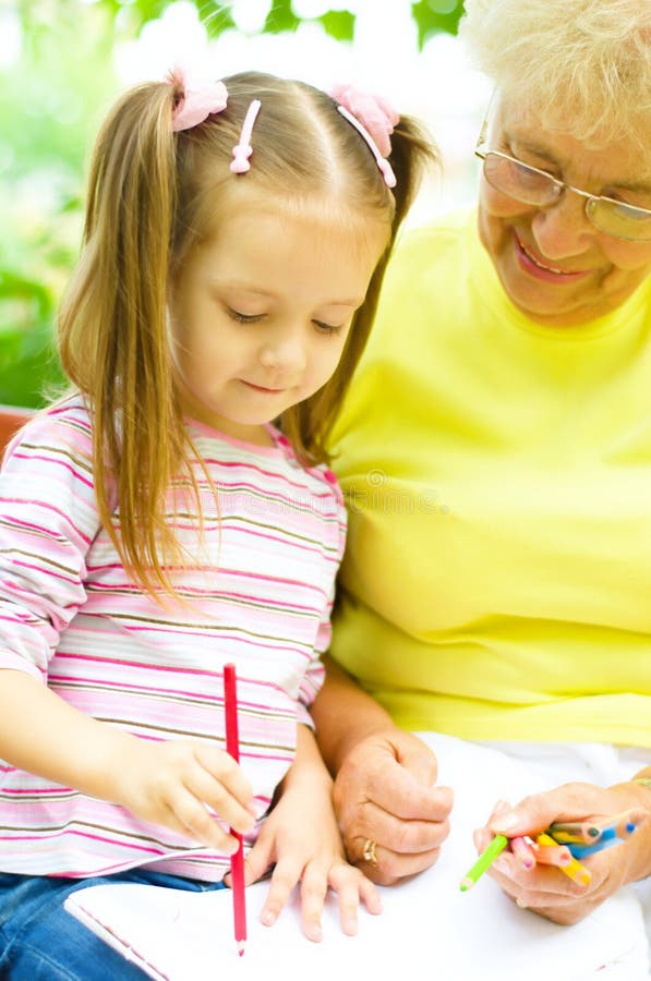 Grandmother with granddaughter drawing. Little girl with her grandmother drawing using crayons outdoors stock images