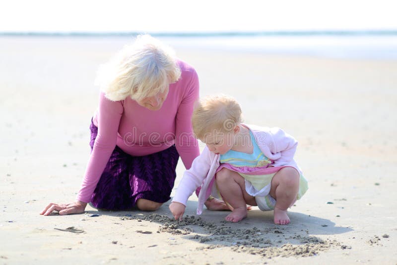 Grandmother and granddaughter playing together on the beach. Happy grandmother playing with her granddaughter, cute toddler girl, at the beach drawing on the royalty free stock photos
