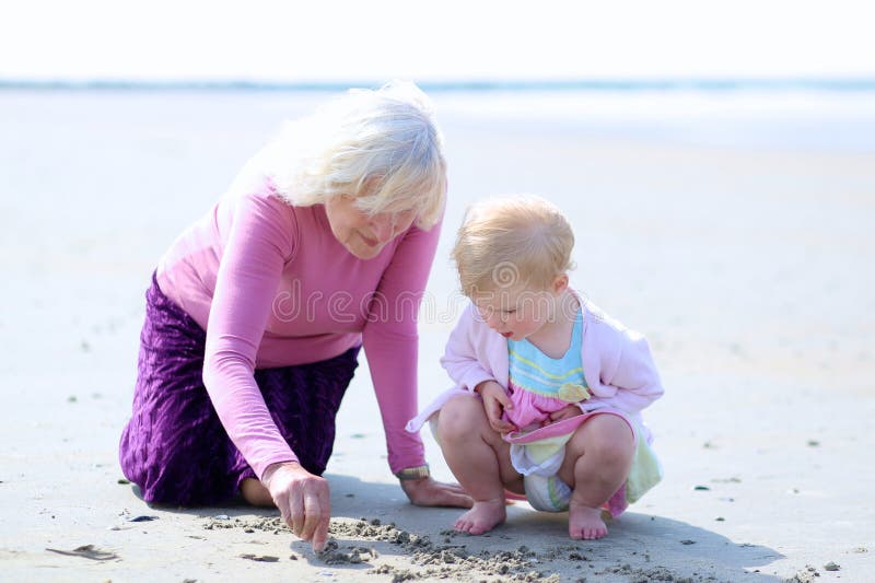 Grandmother and granddaughter playing together on the beach. Happy grandmother playing with her granddaughter, cute toddler girl, at the beach drawing on the royalty free stock images