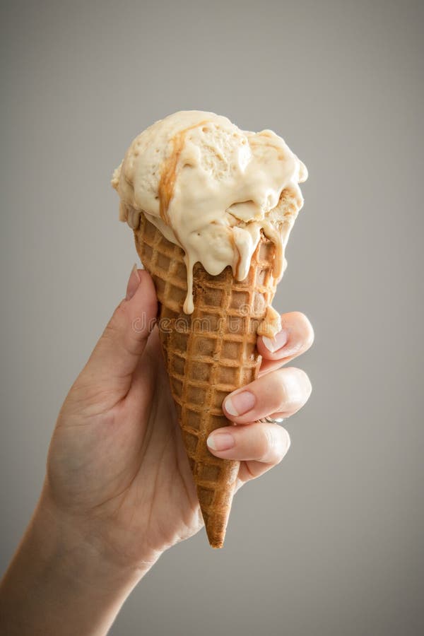 A hand holding a melty caramel ice-cream. Cone with bright background stock photos