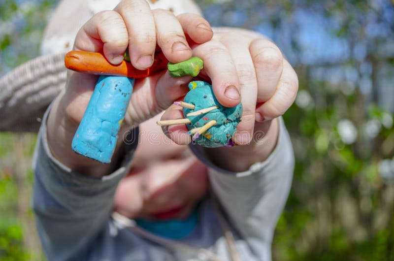 A little boy in panama outside holding blue, green and orange plasticine figures in his hands holding them out in a frame royalty free stock image