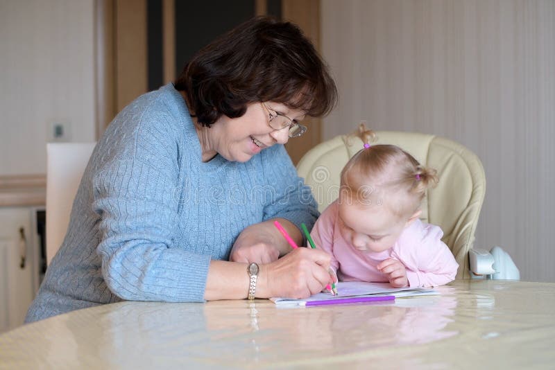 A little girl watches a nanny draw in an album. A child learns to draw. With her grandmother royalty free stock images