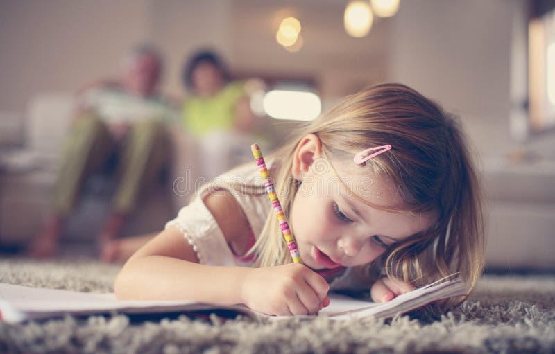 Little girl writing at home. Cute little girl laying on floor and writing. Time for drawing . Little girl with her grandparents stock photography