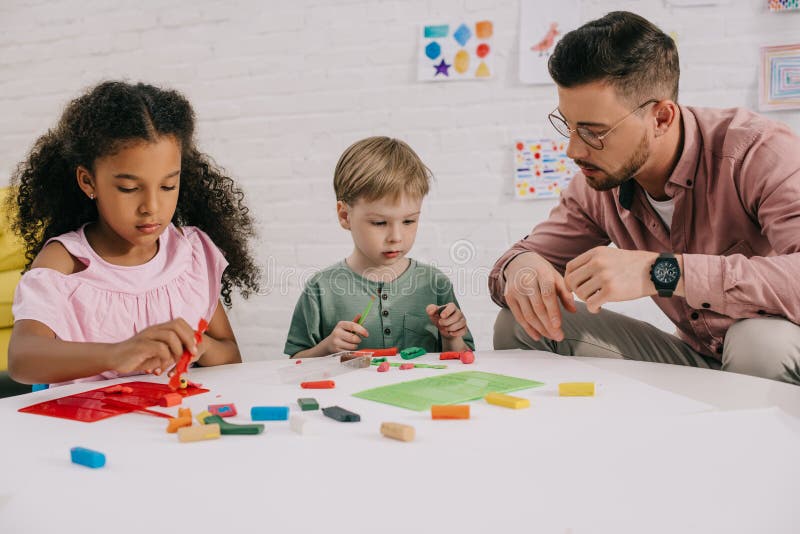 multiracial preschoolers and teacher with plasticine sculpturing figures at table stock photos