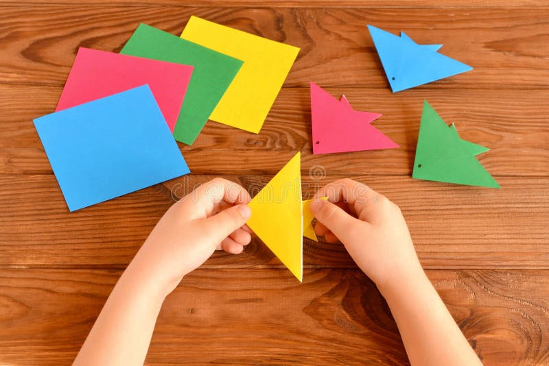 Origami colorful fish, paper sheets, scissors. Child holds paper sheet in his hands and making origami fish stock photo
