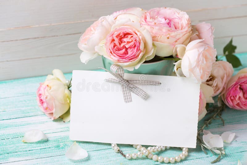 Postcard with sweet roses flowers and empty tag for your text. On turquoise painted wooden background against white wall. Selective focus stock image