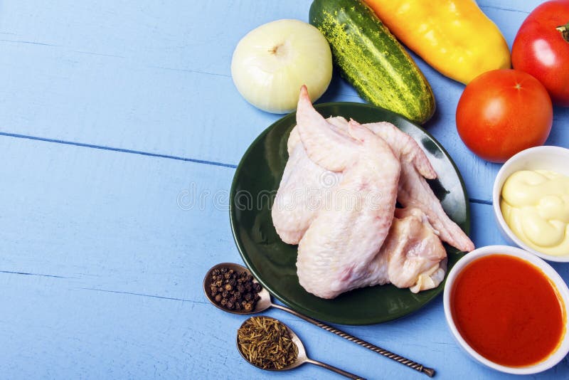 Rustic wooden table with raw ingredients for preparation of natural dish. Chicken wings, mayonnaise, tomato sauce, cucumber, onion. And fragrant spices for stock photography