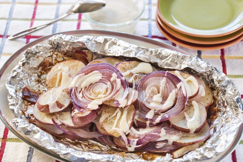 Seasoned red potatoes and onions grilled with bacon. Seasoned red potatoes and onions were grilled with bacon in a foil packet and drizzled with ranch dressing stock image