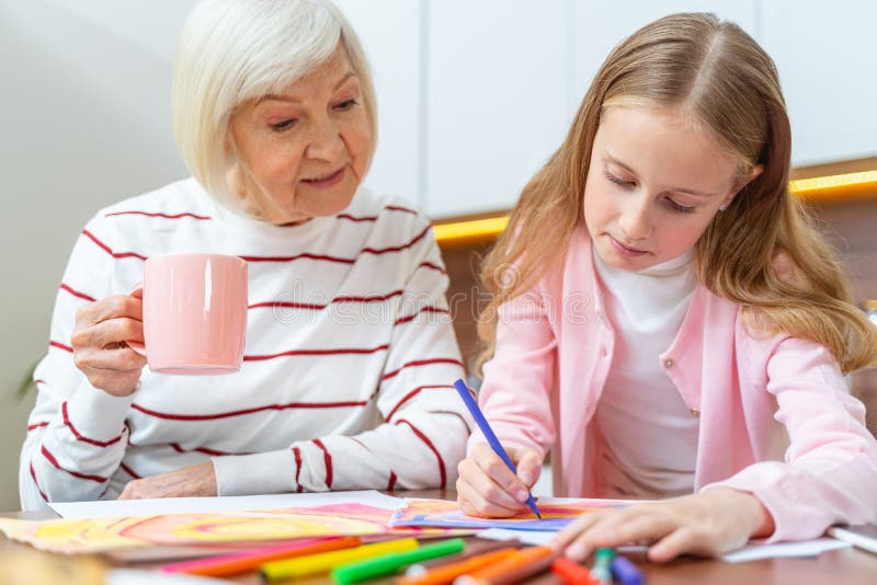 Senior woman gazing at her granddaughters work. Focused girl drawing a picture with a felt pen royalty free stock photography
