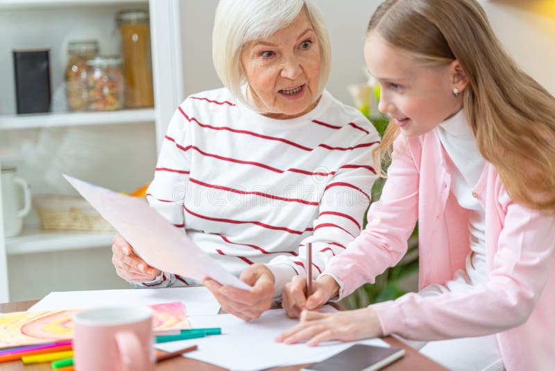 Senior woman teaching her pretty granddaughter drawing. Kid with a pencil in her hand looking at a sheet of paper royalty free stock image