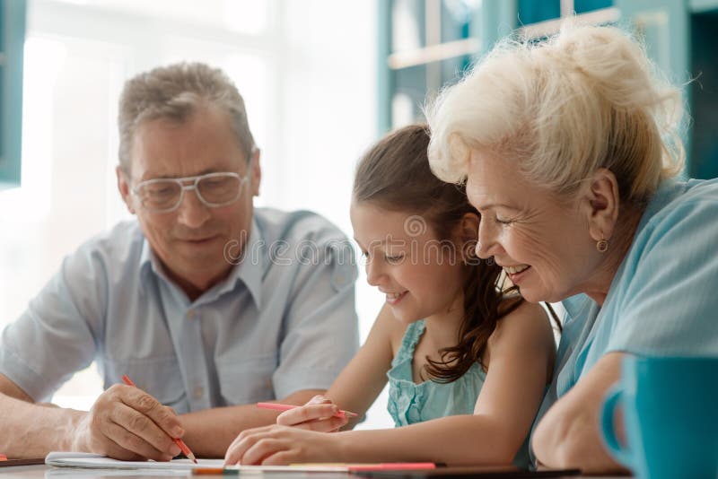 Smiling kid and her grandparents. Family drawing a picture together with color pencils. Happy mood and interesting activity stock images