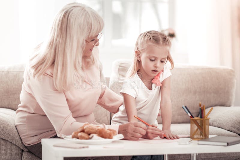 Smiling grandmother drawing pictures with her granddaughter. Time for drawing. Smiling grandmother feeling good while drawing pictures with her granddaughter royalty free stock photos