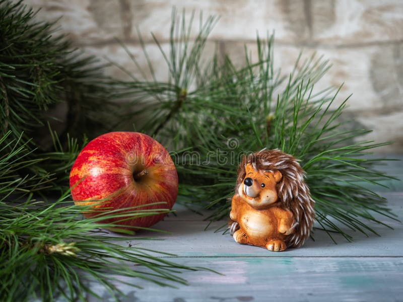 Winter card with a big red apple and a small toy hedgehog cut pine branches on a turquoise wooden background, side view stock photos