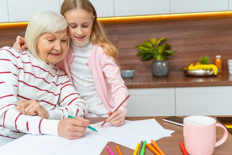 Woman with a felt pen sitting at the table. Girl and her grandmother drawing together on a sheet of paper royalty free stock photo