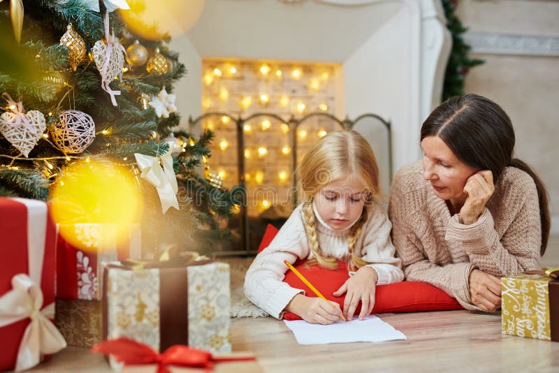 Writing to Santa. Cute little girl writing letter to Santa on xmas night with her grandmother near by stock photography