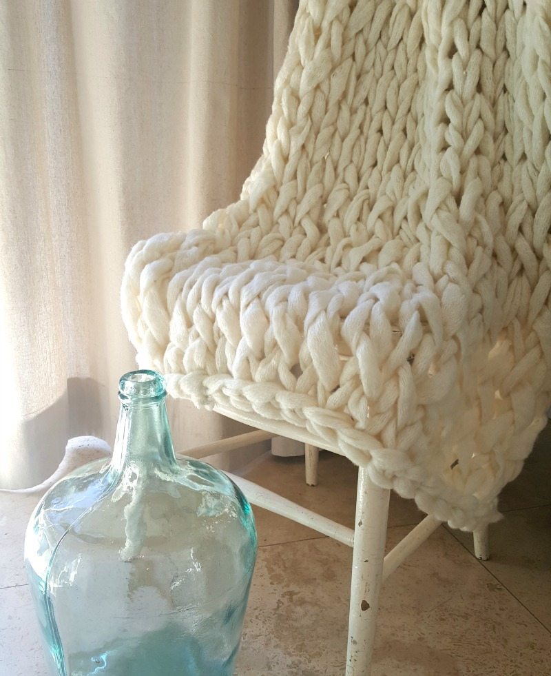 cream colored chunky knit blanket draped over chair with blue vase